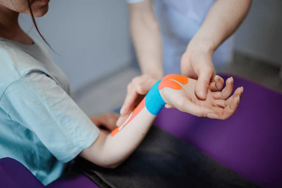 A kinesiologist applies blue and orange kinesio tape to a seated woman’s forearm—ideal for precision personalised kinesiology active rehab and strength and conditioning in Vancouver & Kitsilano.